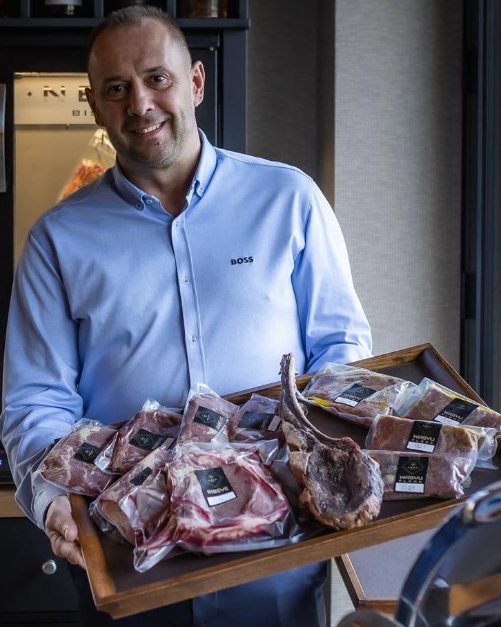 Albert István, a Next Bistro tulajdonosa a húsérlelő szekrény előtt, kezében wagyu és ribeye húsokkal